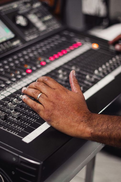 Hand adjusting audio mixer's faders and buttons. Black console with glowing red lights.
