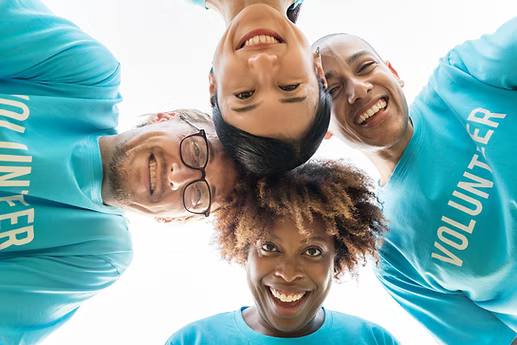 Group of volunteers smiling and looking down, wearing blue shirts.