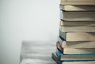Stack of books on a wooden surface, set against a white wall.