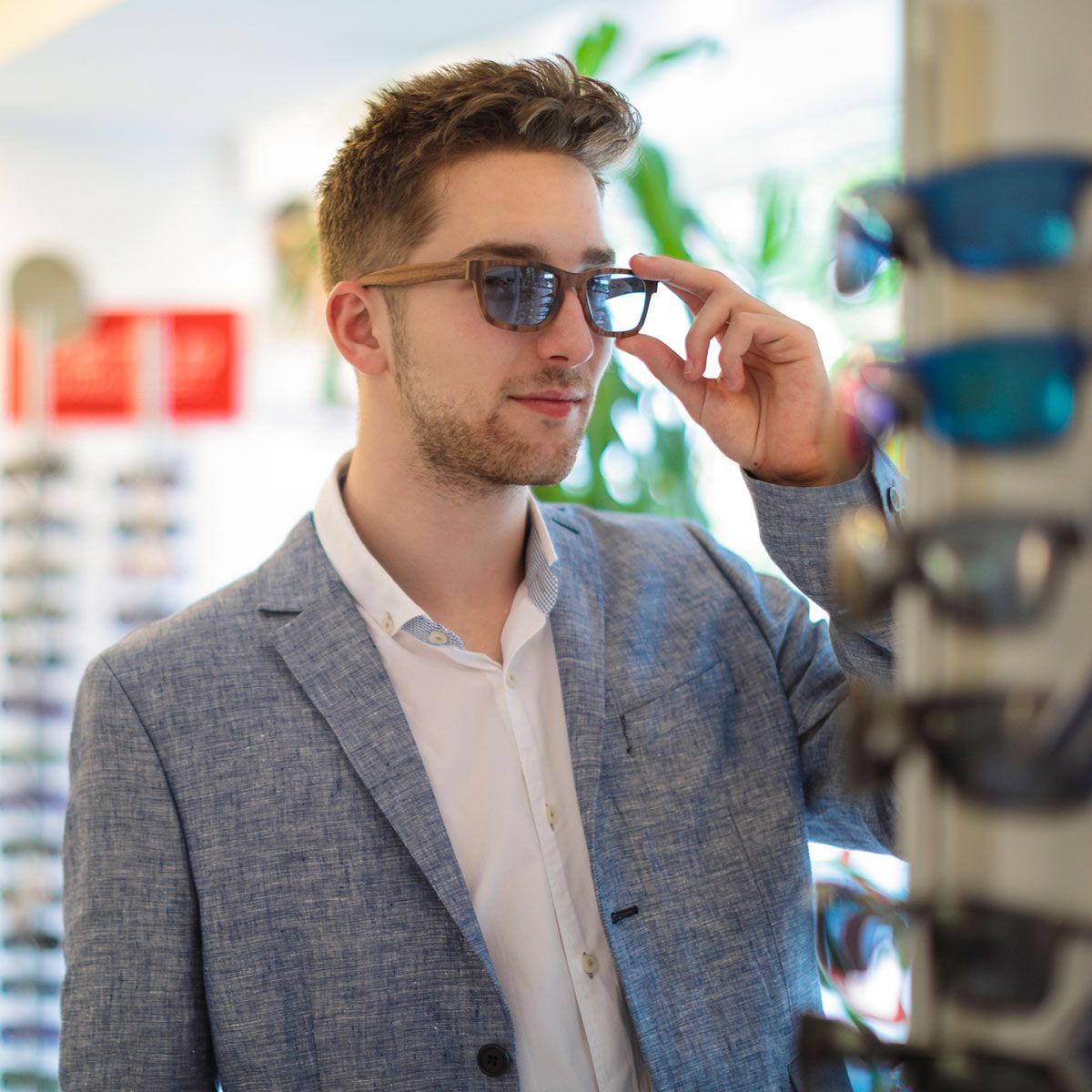 Young man is trying on new sunglasses in the optics store Young man is trying on new sunglasses in the optics store