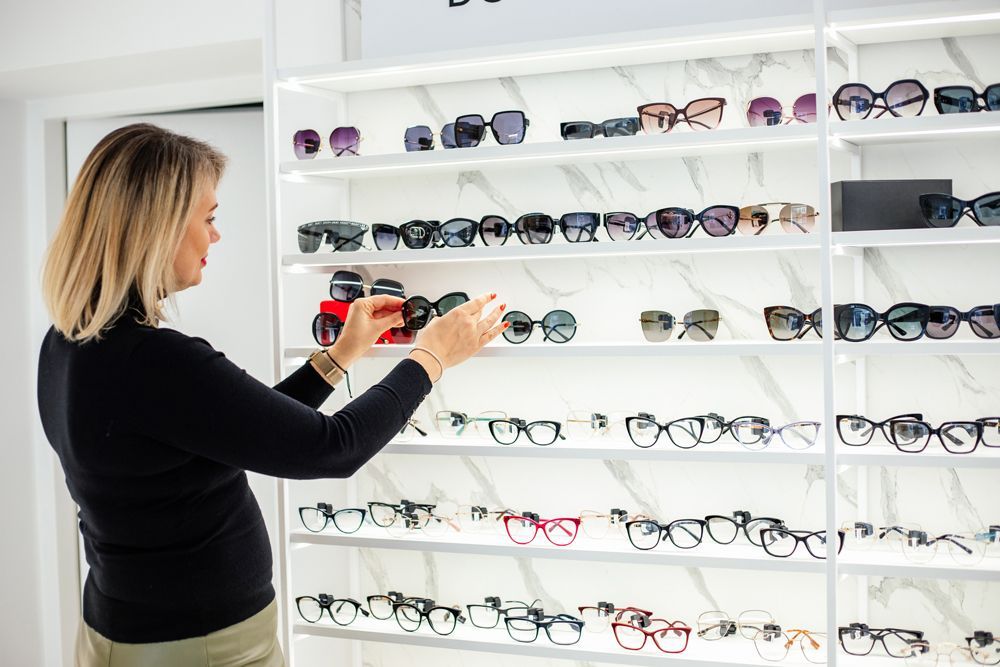 Saleswoman reaching for stylish sunglasses on display in eyewear store, promoting sunglasses. Saleswoman reaching for stylish sunglasses on display in eyewear store, promoting sunglasses.