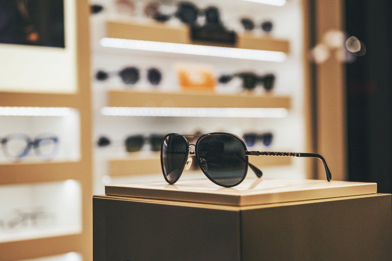 Sunglasses displayed in a store setting, with other eyewear on shelves in the background.