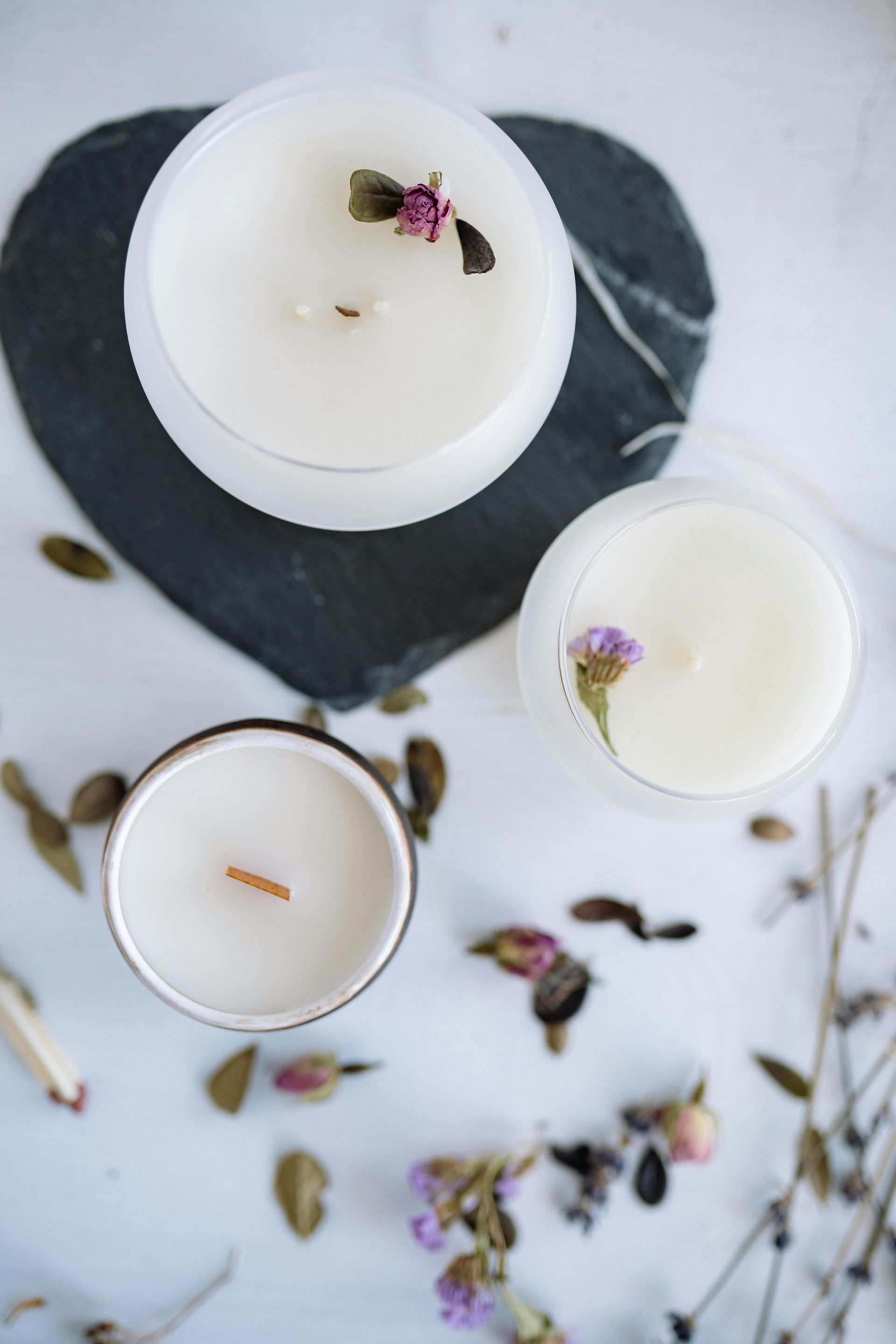 Three lit candles with floral decorations on a heart-shaped stone against a white background.