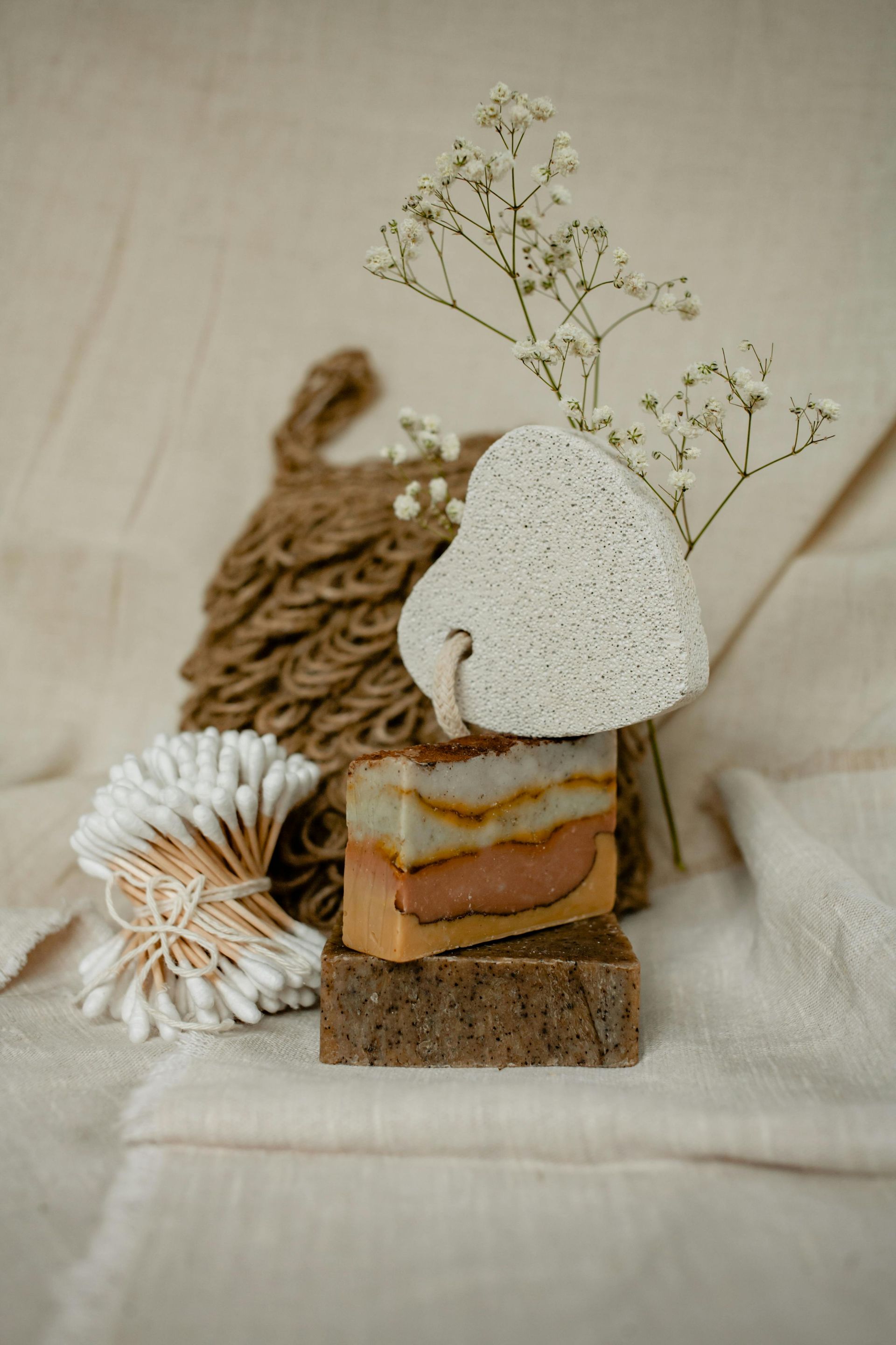 Stacked soaps, pumice stone, and cotton swabs displayed on beige fabric.
