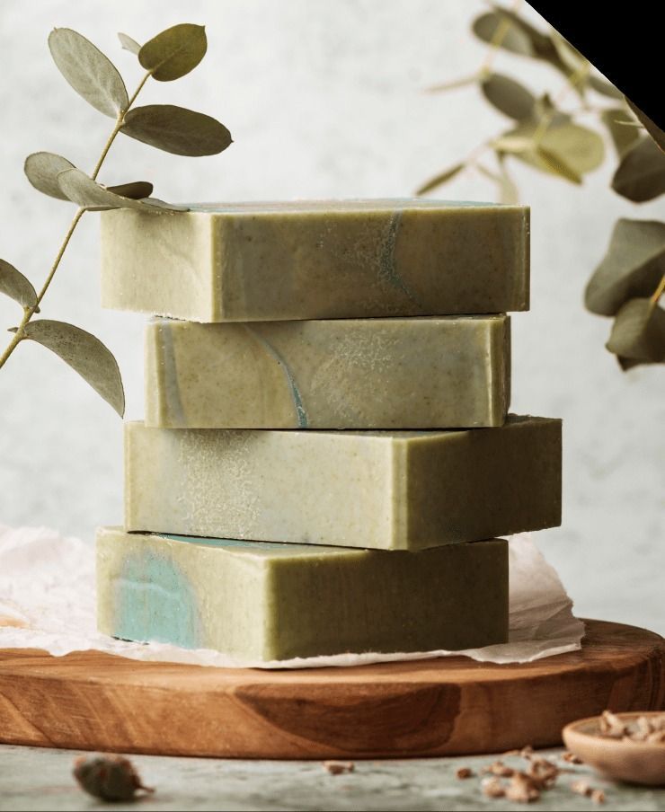 Stack of four green and blue marbled soap bars on a wooden board, with eucalyptus sprigs in the background.