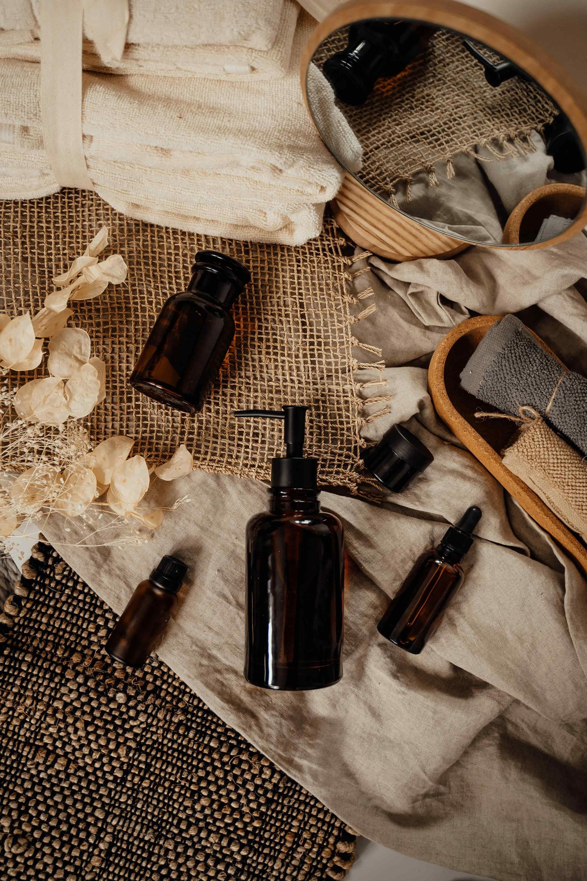 A collection of brown apothecary bottles, a mirror, and linen cloths arranged on a woven surface.