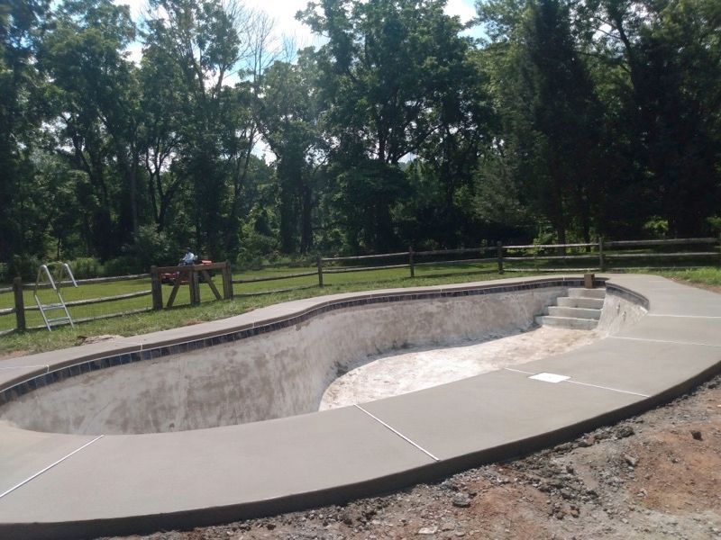 A swimming pool is being built with a concrete walkway around it.