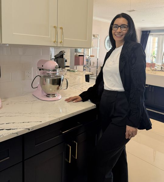 Woman smiling in a kitchen beside a pink stand mixer on a marble countertop.