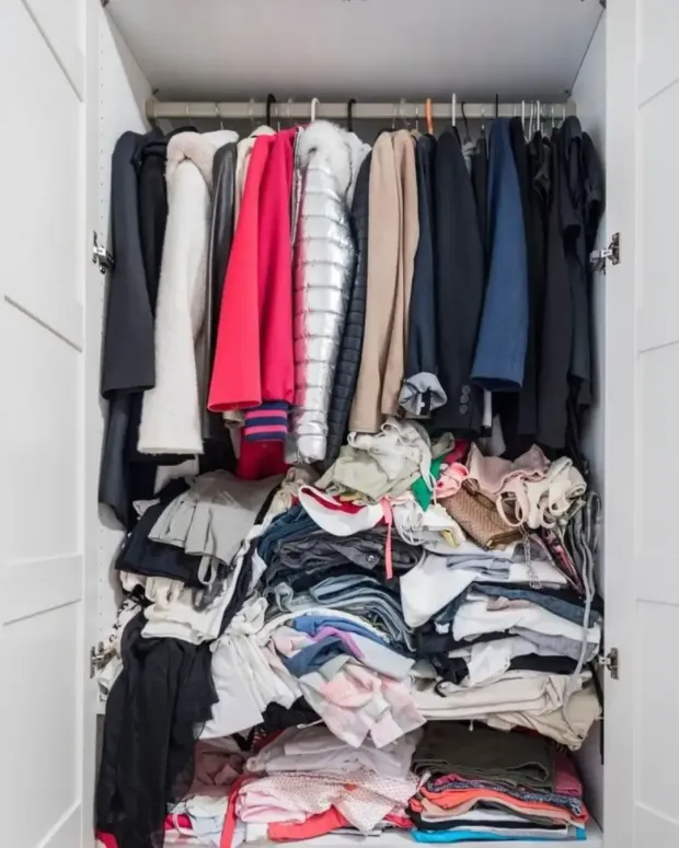 Open wardrobe with hanging coats and folded clothes piled on the shelves.