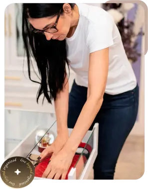 Woman packing clothes into a suitcase on a bed, wearing glasses and a white shirt.