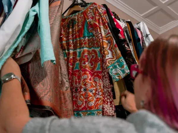 A woman with pink hair is looking at clothes in a closet.