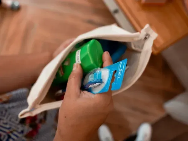 A person is holding a bag of toothpaste and a toothbrush in their hand.