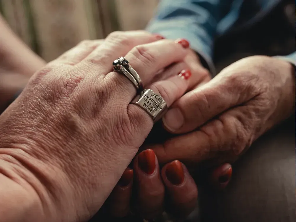 2 people are holding hands with rings on their fingers.