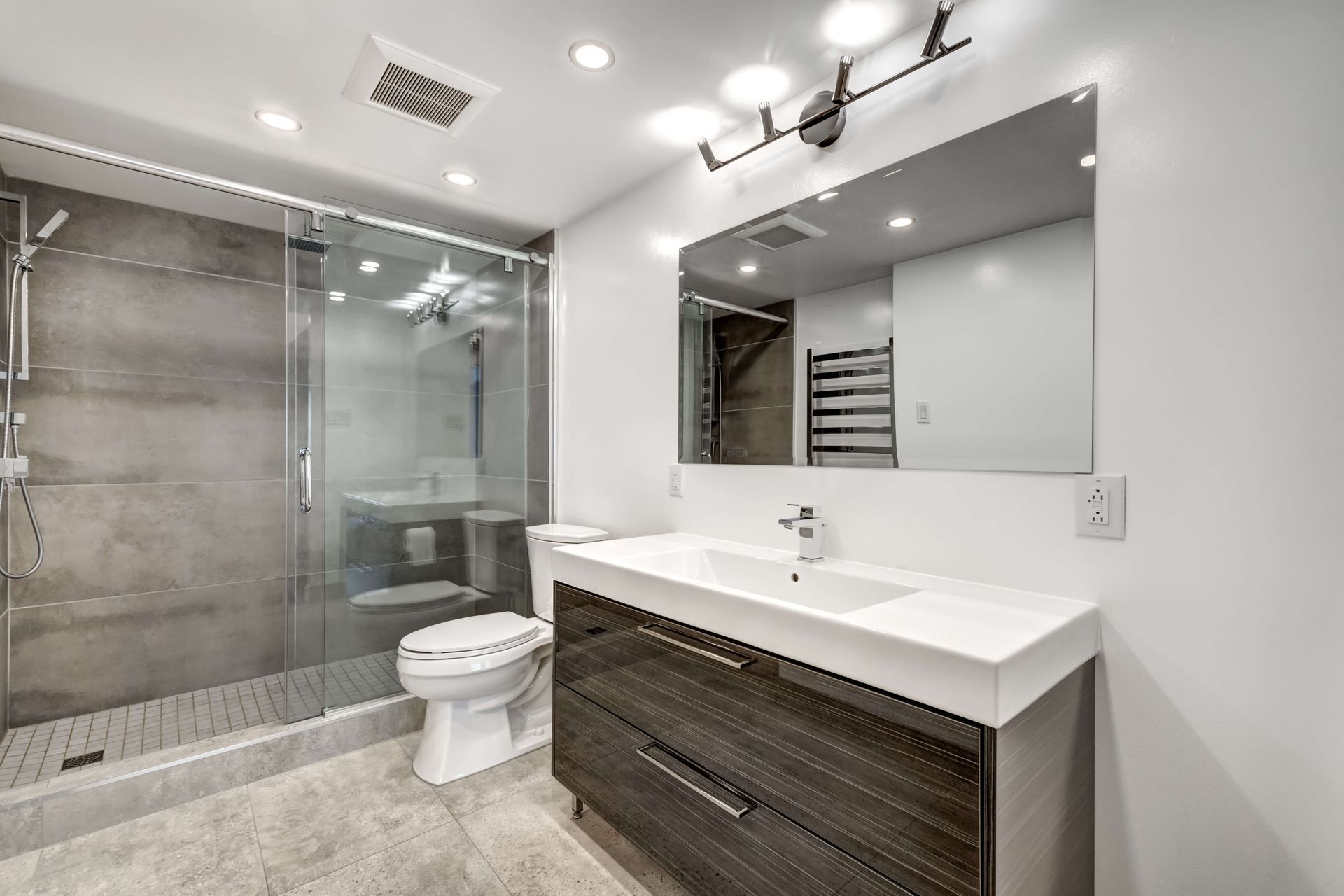 Modern bathroom with glass shower, white vanity, large mirror, and toilet.
