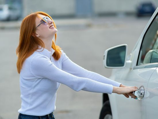 A woman is trying to open the door of a white car.