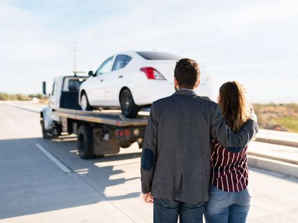 A man and a woman are standing next to a tow truck with a car on the back.