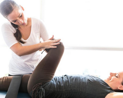 A woman is stretching another woman 's leg on a table.