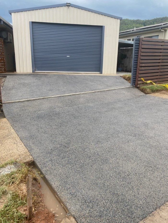 A Concrete Driveway Leading To A Garage With A Blue Garage Door — Core Concrete in Cairns, QLD