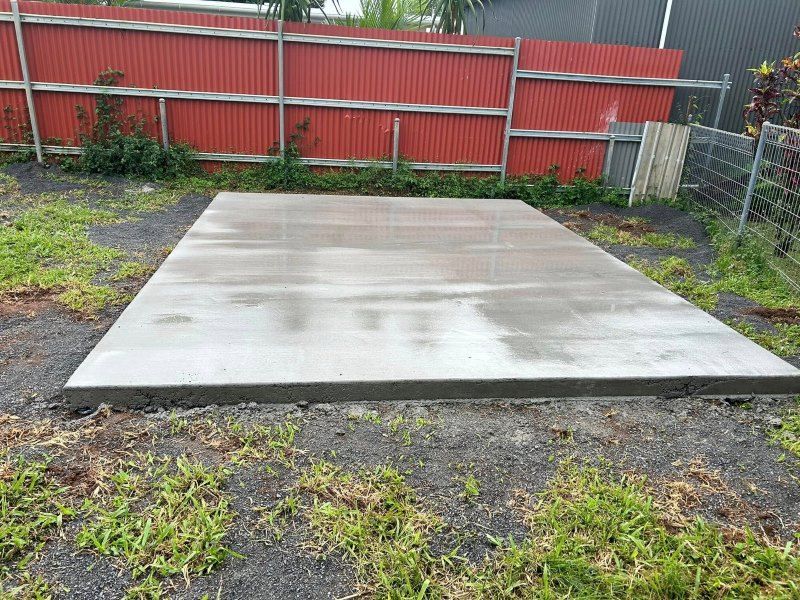 A Large Concrete Slab is Sitting in the Grass in Front of a Red Fence — Core Concrete in Port Douglas, QLD
