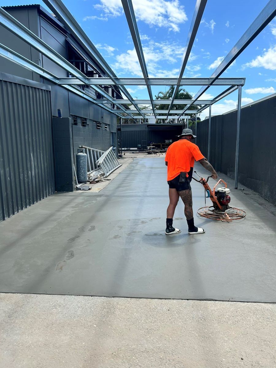 A Man In An Orange Shirt Is Standing On A Concrete Floor — Core Concrete in Cairns, QLD