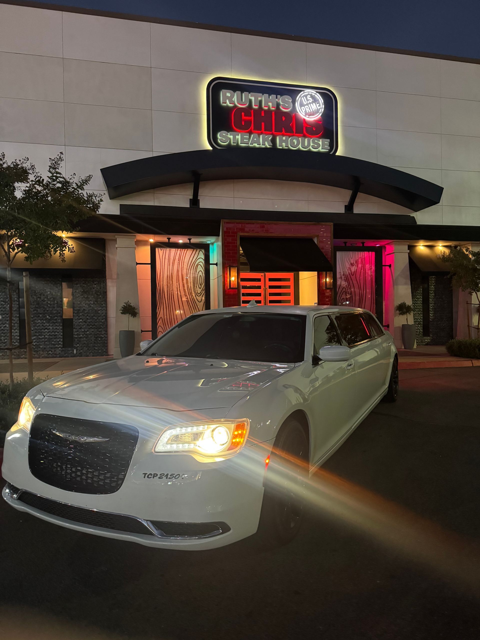 White Chrysler 300 parked in front of Ruth's Chris Steak House at dusk; illuminated sign.