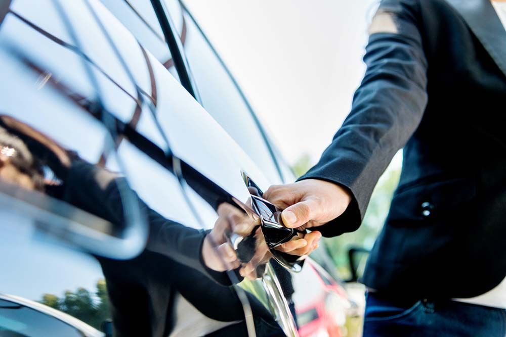 Person in a black blazer opening a black car door.