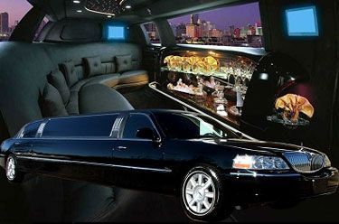 Black limousine, interior view with seating, bar, and city skyline visible through the windows.