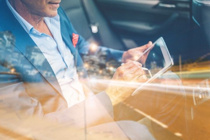 Man in suit using a tablet in a car, city lights blurred in the background.