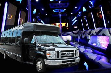 Black party bus interior with neon blue lights and pole.