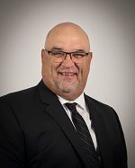 Bald man with glasses wearing a black suit and tie, smiling.