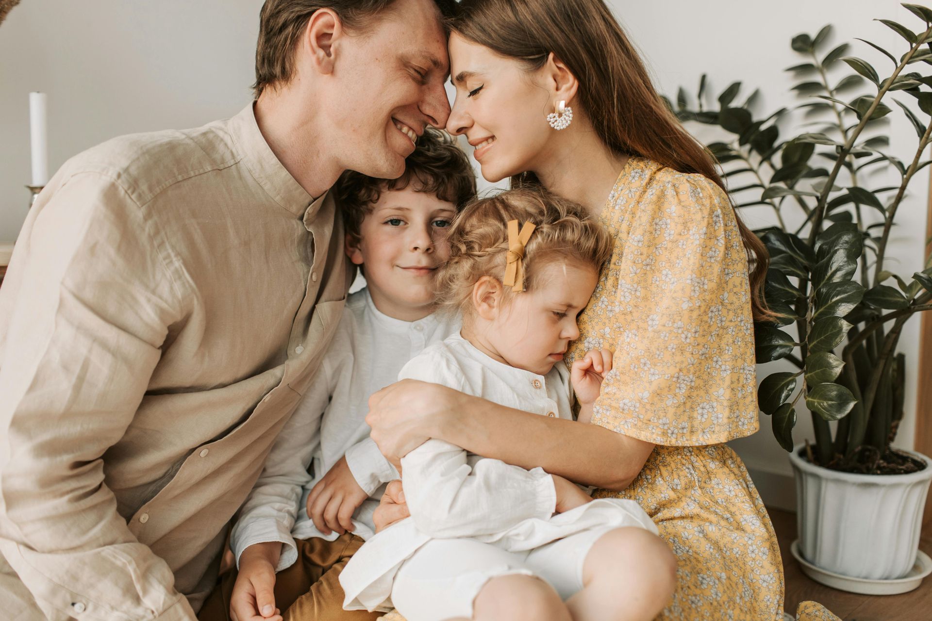 Family of four smiling and embracing indoors; includes parents and two children.