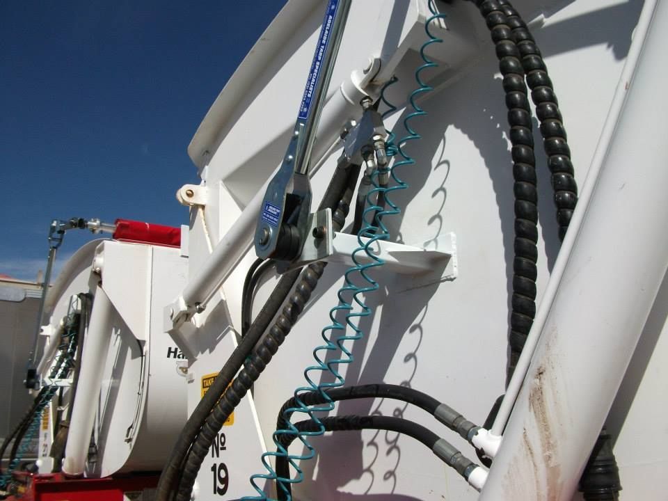 White waste disposal truck with black hoses against a blue sky.