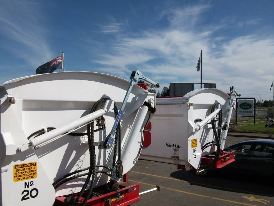 White garbage truck compartments with hydraulic arms; New Zealand flags in background.