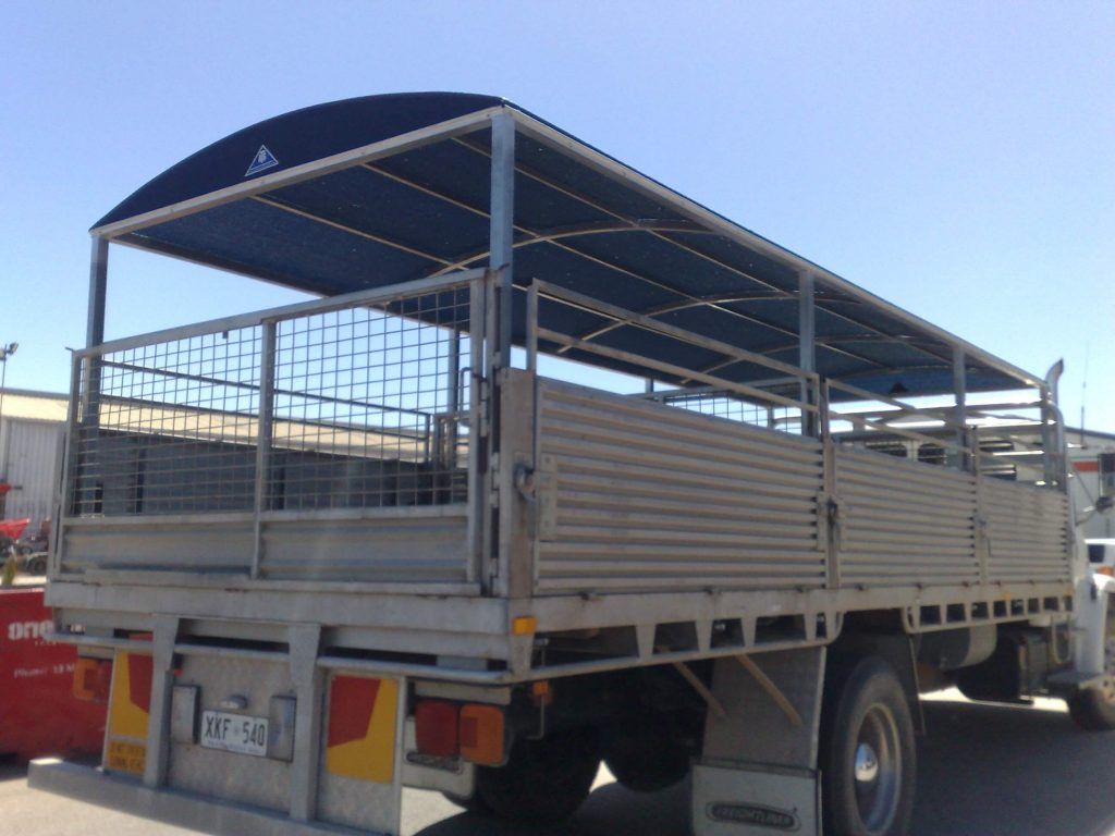 Rear view of a truck with a caged, covered bed, likely for transporting animals, under a blue sky.