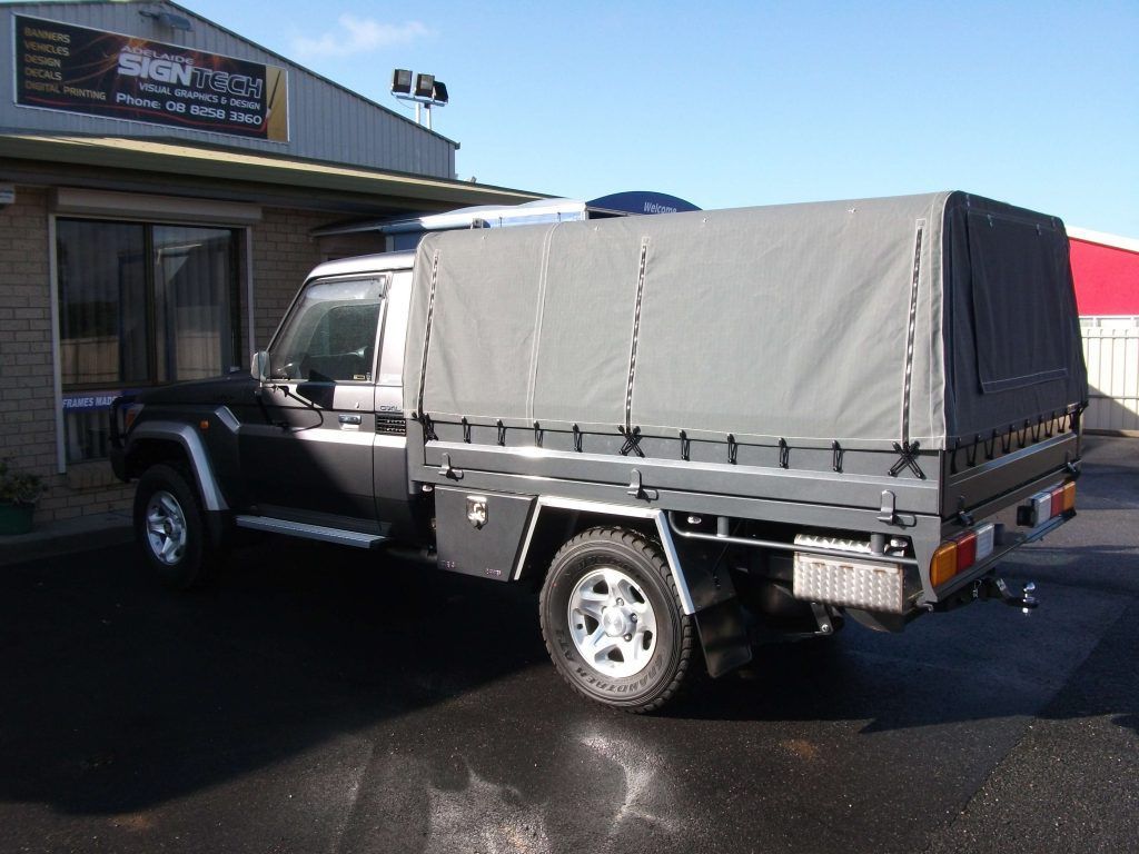 Dark grey pickup truck with a grey canopy parked outside a building.