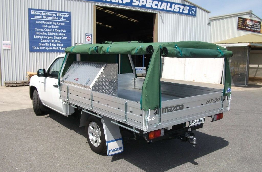 White Mazda truck with aluminum tray, green canvas canopy, parked outside a workshop.