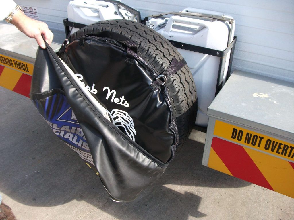 Person holding open a black tire cover. Two white fuel cans and a tire are visible in the background.