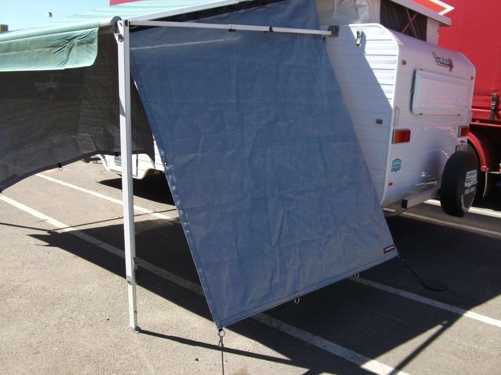 A camper with an attached gray sunshade, set up on asphalt.
