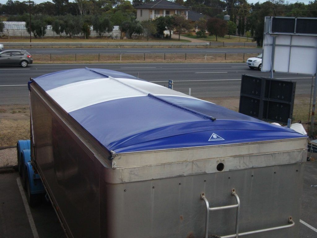Blue and white tarp roof on a metal trailer parked next to a road.
