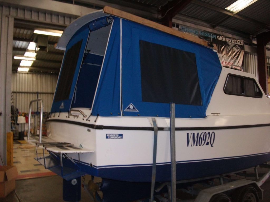 A blue and white boat with a blue canvas enclosure, parked in a garage.