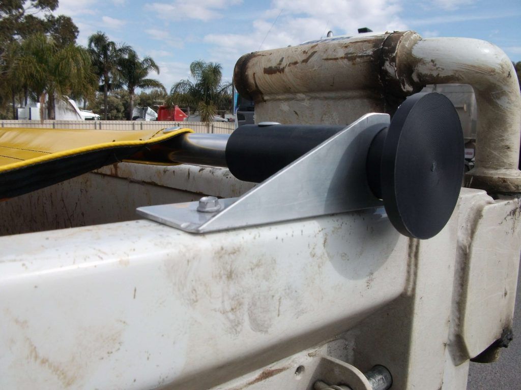 Metal bracket with a black roller mounted on a white industrial machine.