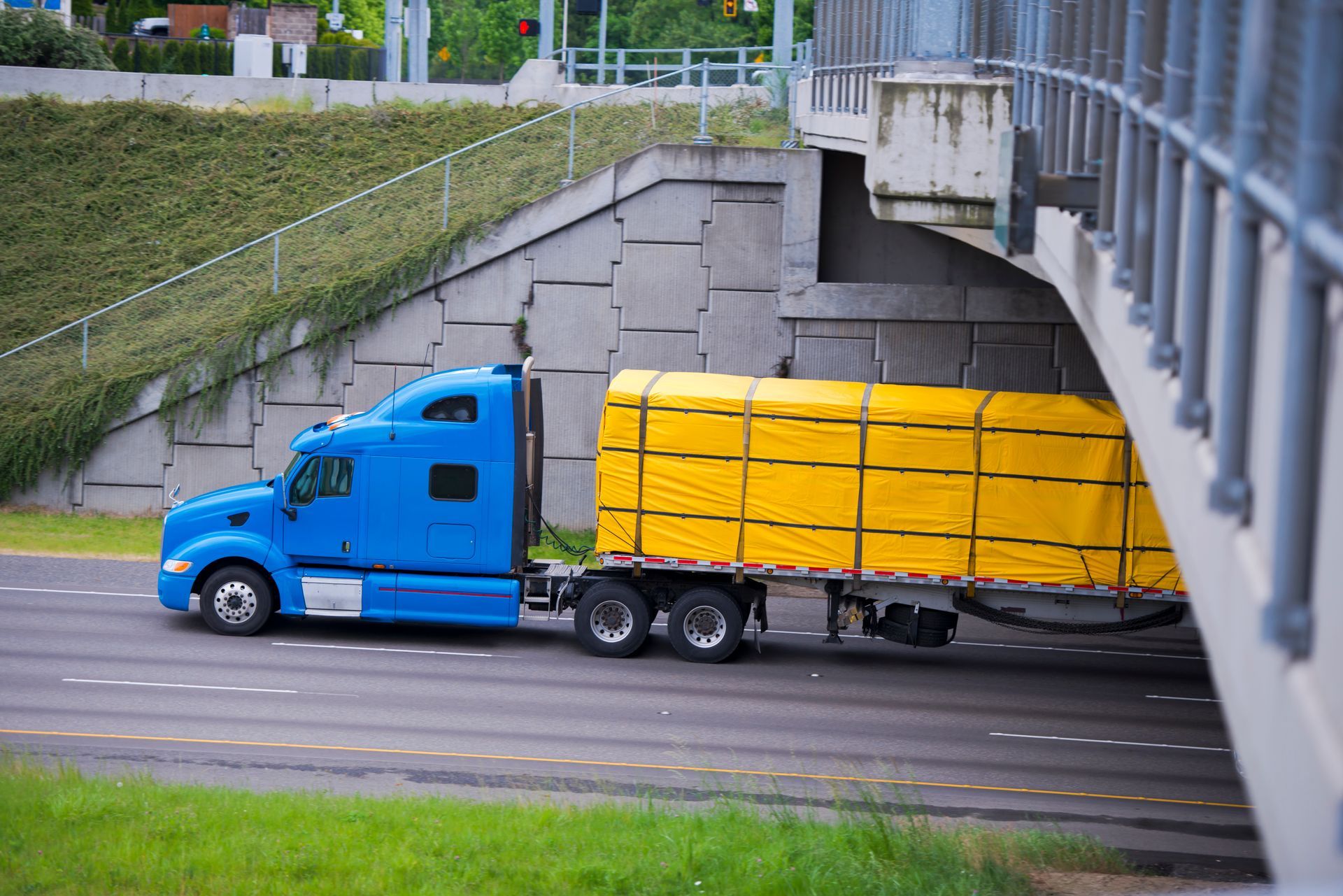 Yellow semi-truck with covered trailer driving on a highway.