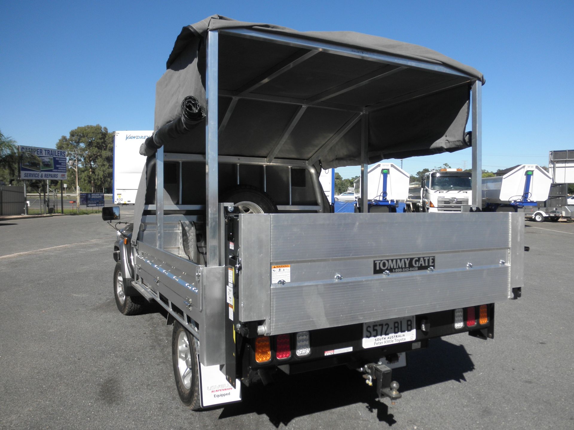 Silver utility truck with gray canopy, parked outside on a sunny day.