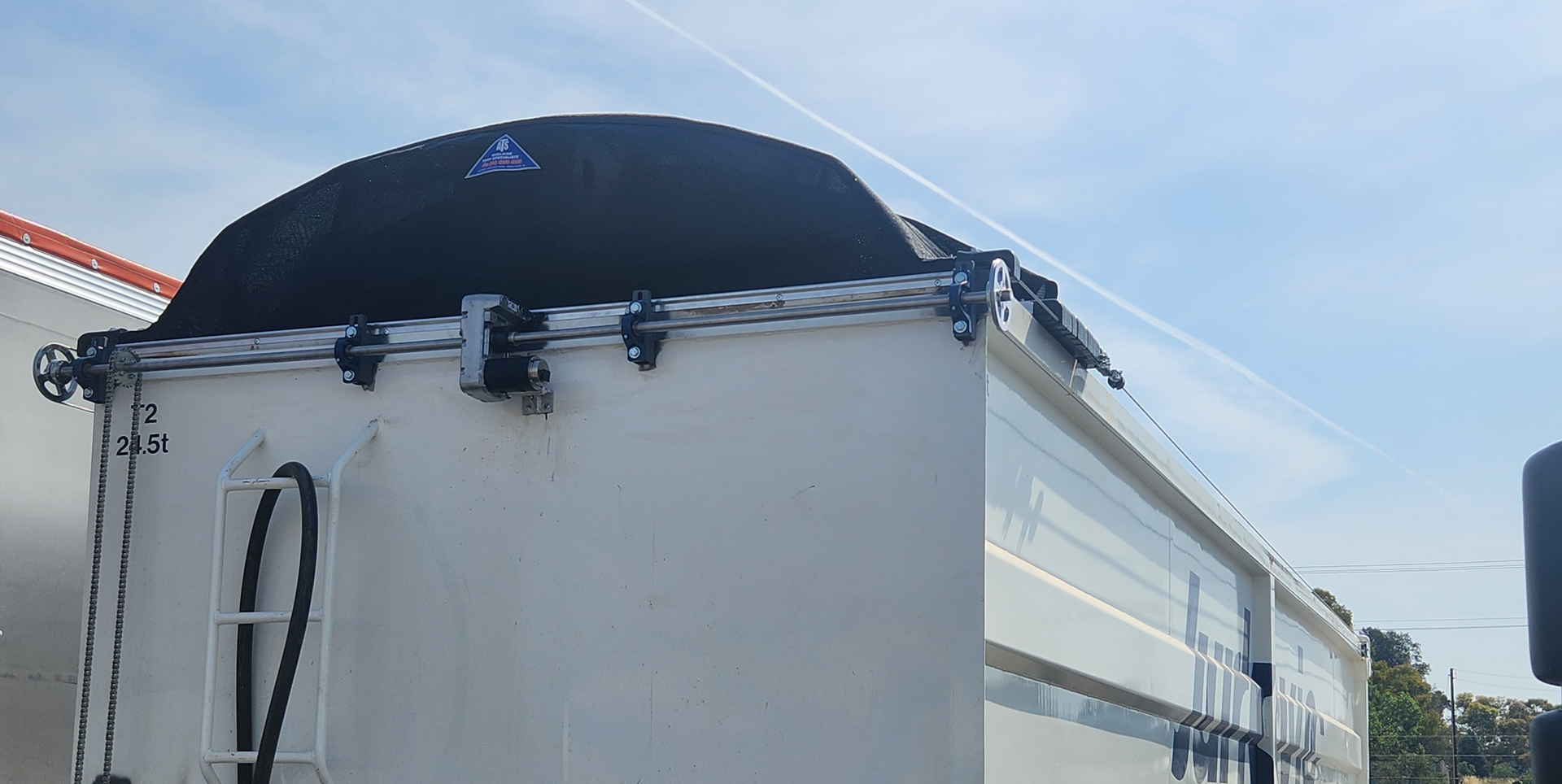 Black covered trailer top with white sides against a blue sky.