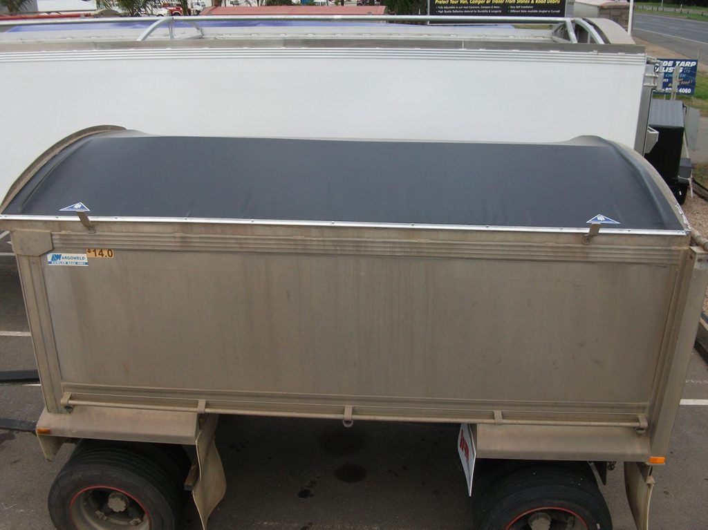 A dusty, silver trailer with a black tarp roof parked in a lot.