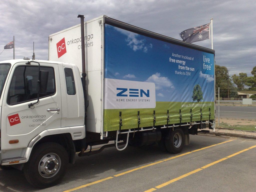 White truck with blue and green advertisement banner for ZEN. Parked outdoors.