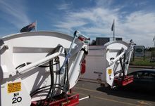 Two large white garbage trucks with raised arms, outdoors.