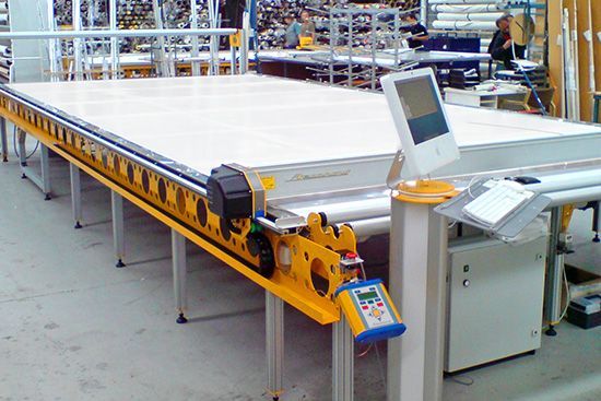 Industrial conveyor machine with a large white sheet and yellow frame in a factory workshop