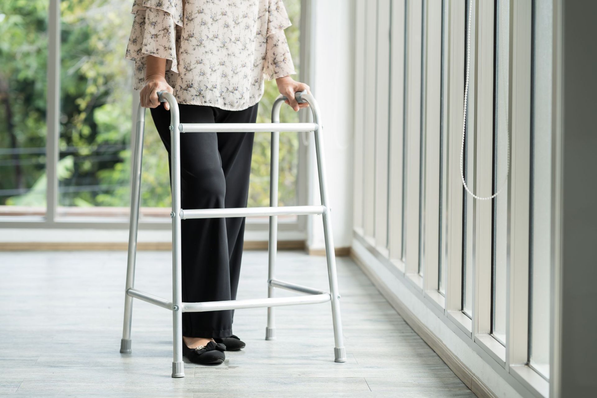 Woman using a walker indoors near a large window.