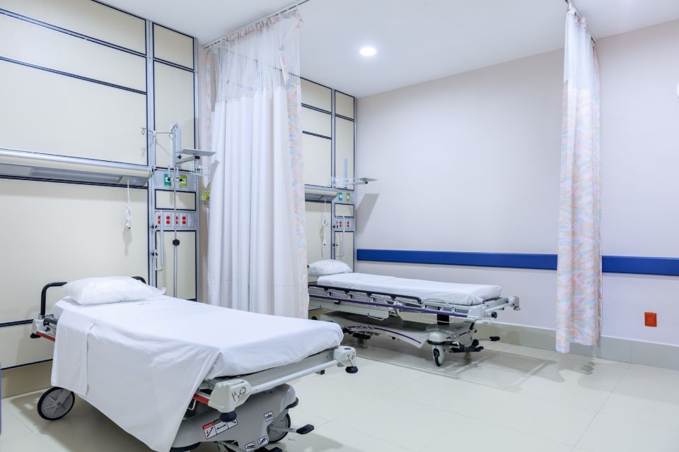 Two hospital beds in a bright, clean room with white curtains and medical equipment.